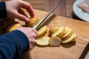 Potatoes being sliced thinly on a chopping board